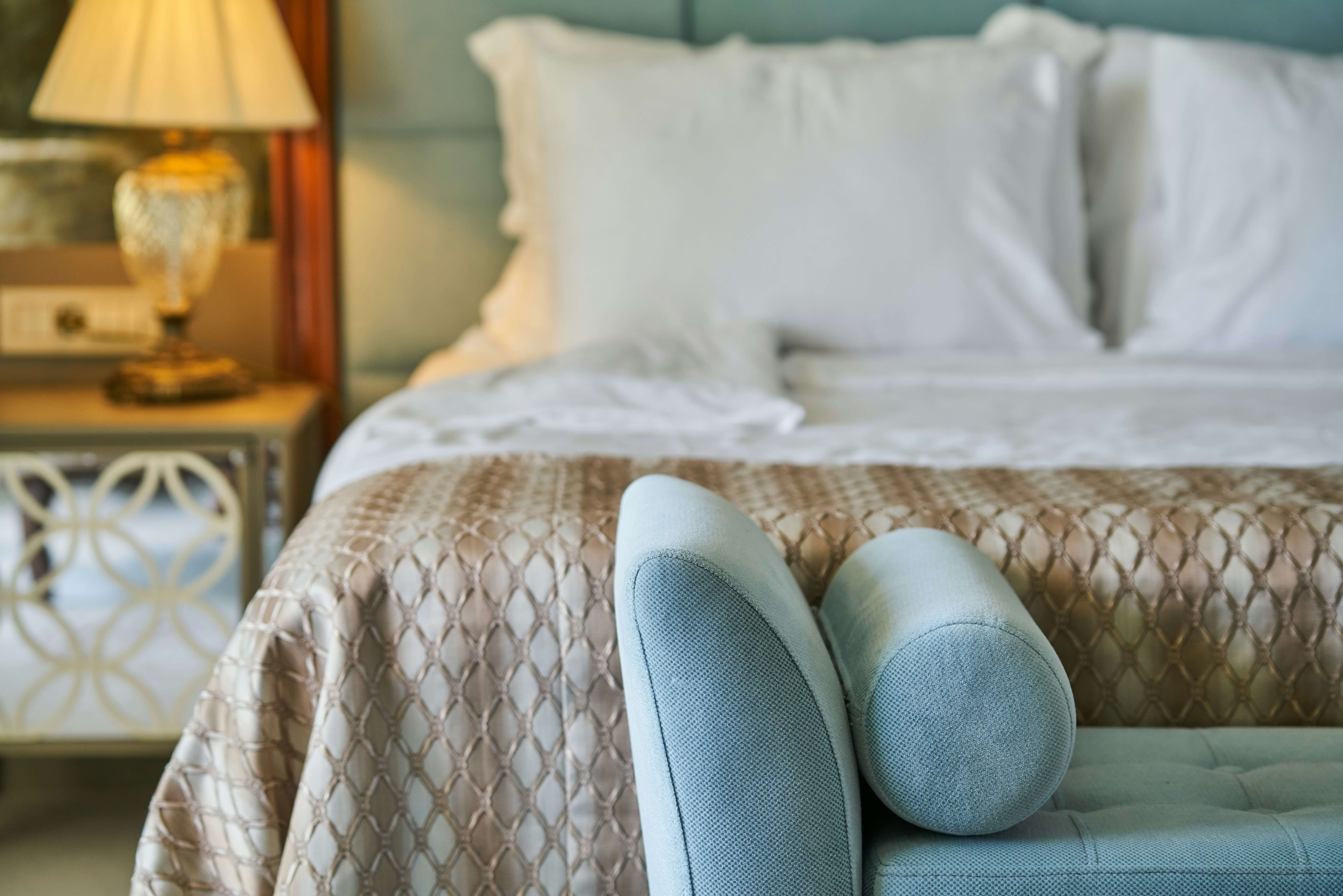 a hotel bed, chair and bedside table in a luxury suite